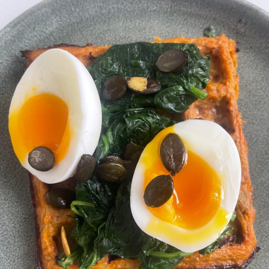 Une gaufre de patate douce garnie d'épinards fondus, de deux moitiés d'œuf mollet et de graines de courge, préparée par Anaïs